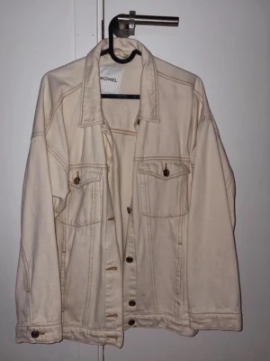 Beige jeansjacka från Monki - Stilren beige jeansjacka från Monki med klassisk krage, bröstfickor med knappar och knappstängning framtill. Oversized passform och snygga söm-detaljer. 