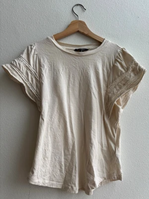 Topp/blus från Lauren - Ralph Lauren  - Söt cremefärgad topp från Lauren - Ralph lauren i mycket bra skick. Använd endast en gång. LACE TRIM JERSEY FLUTTER SLEEVE TOP - T-shirt - bas - mascarpone cream