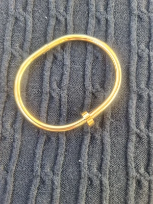 Guldigt armband i minimalistisk nail design - Snyggt armband i guldfärgad metall med en stilren och modern form. Armbandet har en unik böjd design med en liten detalj som liknar en skruv. Perfekt för dig som gillar enkel och trendig stil.