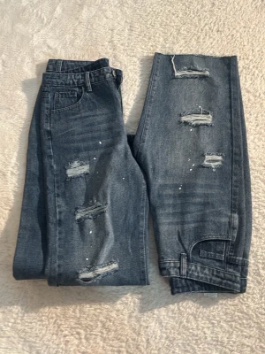 Dubbelpack shorts och jeans. DEAL!! - Säljer ett par grå jeansshorts med slitnabyxor 2 in 1 med  detaljer och hål på framsidan. Shortsen har fem fickor, knapp och dragkedja i midjan samt en avslappnad passform. Perfekta för en cool och avslappnad stil.