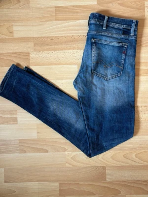 Replay Jeans - Blåa  - Replay jeans i snygg mellanblå tvätt med tydliga fades och slitningar som ger den där klassiska Replay-looken.  Modellen har en smal passform med stretch för hög komfort och en modern silhuett. Perfekta för dig som gillar jeans med karaktär och en välanvänd premiumkänsla.  ✔️ Original Replay ✔️ Mellanblå tvätt med snygga slitningar ✔️ Slim fit passform ✔️ Stretchig och bekväm ✔️ Fint använt skick  Passar lika bra till sneakers som boots och är enkla att matcha med både hoodie, t-shirt och skjorta.  