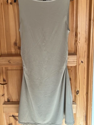 Beige ärmlös långklänning - Stilren beige långklänning i ett mjukt, stretchigt material. Klänningen är ärmlös och har en enkel, rak passform som faller snyggt längs kroppen. Perfekt för dig som gillar minimalistisk och clean stil.
