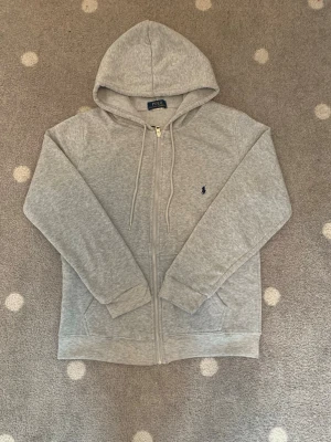 Grå zip hoodie från Polo Ralph Lauren - Grå Pullover Fleece Zip-Up – Storlek S  Säljer en grå pullover fleece med zip-up i storlek S. Tröjan är i nyskick, knappt använd och utan några skador eller fläckar.  Den har ett mjukt och skönt fleecematerial på insidan, vilket gör den väldigt varm och bekväm att ha på sig. Perfekt till både vardags och kallare dagar.  Skick: Nyskick / knappt använd Storlek: S Pris: 700 kr Vid snabb affär: 500 kr  Skicka gärna ett meddelande om du har några frågor eller vill ha fler bilder!