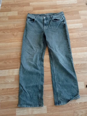 Gråa Jeans - Säljer ett par gråa jeans med rak passform och klassisk femficksdesign. Jeansen har normal midja och är tillverkade i denim. Perfekta för en avslappnad och stilren look.