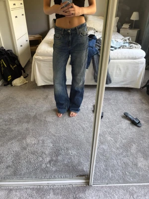 Blå baggy jeans med raka ben - Säljer ett par blå baggy jeans med raka ben och låg midja. Jeansen har klassiska fem fickor och slitningar för en avslappnad look. Perfekta för dig som gillar en loose fit och vintagekänsla. Materialet är denim i bomull.