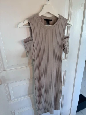 Beige ribbad klänning Forever 21 - Säljer en beige ribbad klänning från Forever 21 med cut out-detaljer vid axlarna. Klänningen har en rak passform och är tillverkad i ett mjukt, stretchigt material. Perfekt för dig som gillar stilrena och trendiga plagg.
