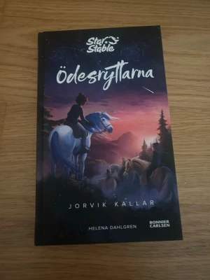 Star Stable Ödesryttarna: Jorvik Kallar - En spännande bok av Helena Dahlgren från serien Star Stable, 'Ödesryttarna: Jorvik Kallar'. Omslaget har en magisk illustration med hästar och en tjej i solnedgång. Perfekt för dig som gillar äventyr, vänskap och magi i en fantasifull värld.