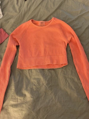 Ribbad orange croppad topp Aim'n - Snygg ribbad croppad topp från Aim'n i orange. Långärmad modell med rund hals, tillverkad i stretchigt material med 92% polyamid och 8% elastan. Perfekt för dig som gillar sportig och trendig stil.