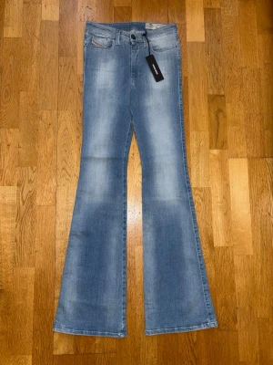 Ljusblå bootcut jeans med utsvängda ben - Säljer ett par ljusblå bootcut jeans med utsvängda ben och klassisk femficksmodell. Jeansen har en snygg tvätt med slitningar på låren och knäna. Perfekta för dig som gillar retrovibbar och vill ha ett par jeans som sticker ut.