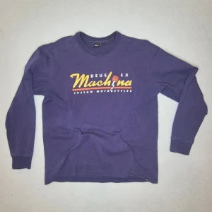 Deus Ex Machina - Långärmad tröja/sweatshirt från Deus Ex Machina med “Machine – Custom Motorcycles”-tryck framtill.  Snygg mörkblå färg med retro motorcykel-/garagekänsla.  Passar bra till jeans, workwear, streetwear eller som casual vardagströja.  Märke: Deus Ex Machina Storlek: L Färg: Mörkblå Tryck: Machine / Custom Motorcycles Skick: måttligt använd. Inga fel vad jag kan se. Skick utifrån bilder.   Mått: Bröstbredd: ca 58 cm Längd: ca 69 cm från armhåla till ärmslut: ca 53 cm Bredd/axel ungefär: ca 53 cm