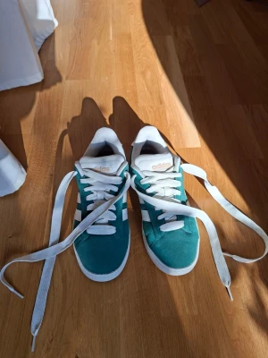 Sneakers dam strlk 39 Adidas Original i grön mocka med vita detaljer  - Klassisk sneaker med "cloud foam". Den gröna färgen har litet dragning åt blågrått. En aning tyngre än Adidas "Gazelle", men skillnaden är liten. Köpta i mars -26 och använda i ca 1 timme. Liten grön fläck på ena skobandet. Mycket ytlig förslitning på ena skosulans framdel. Annars inga defekter.