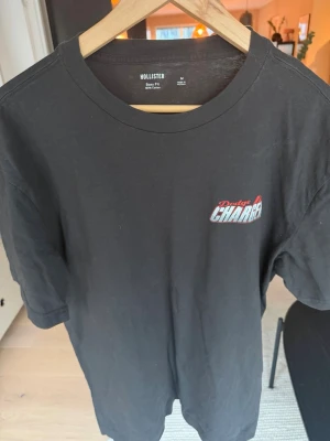 Svart Dodge Charger t-shirt Hollister - Svart t-shirt från Hollister med boxy fit och trycket 'Dodge Charger' på bröstet. Tillverkad i 100% bomull och har en klassisk rund halsringning samt korta ärmar. Perfekt för dig som gillar bilar och streetwear.