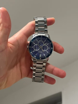 Regal klocka 46mm - Snygg klocka med blå urtavla och flera små urtavlor för extra funktioner. Klockan har ett robust metallarmband i silverfärg och en rund boett. Perfekt accessoar för dig som vill ha en modern och stilren look.