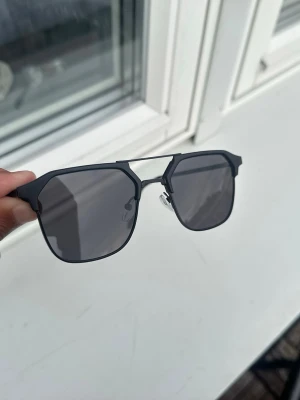 Herr solglasögon - Snygga solglasögon med svart metallbåge och mörka, fyrkantiga linser. Modern design med dubbla bryggor och tunna skalmar. Perfekta för dig som vill ha en stilren och edgy look i solen.