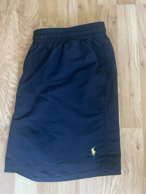 Marinblå badbyxor från Polo Ralph Lauren - Snygga marinblå badbyxor från Polo Ralph Lauren med klassisk gul logga broderad på benet Äkta använda 1 gång sen ändrar mig .  strl xxl men mer L väger 90 passar perfekt 