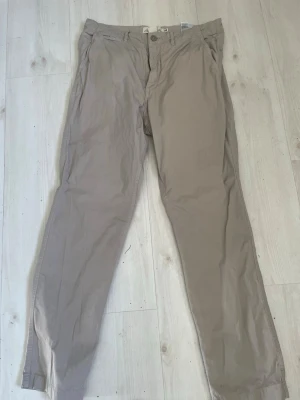 Beige chinos med rak passform - Snygga beige chinos med rak passform och klassisk design. Byxorna har sidofickor och bälteshällor i midjan. Tillverkade i ett lätt och bekvämt bomullsmaterial som passar perfekt till en avslappnad stil.