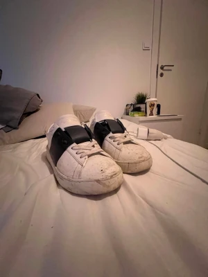 Vita sneakers från Valentino - Säljer ett par vita sneakers från Valentino Garavani med bred svart rem över mitten. Skorna har klassisk låg profil, vita snören och är tillverkade i läder. Snygg och stilren design som passar till det mesta. Tvättar såklart innan och priset är inte hugget i sten. och det mesta är smuts som går att ta bort.