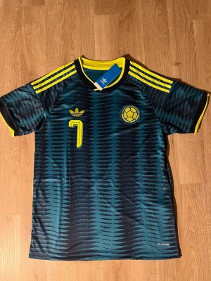 Colombia VM-fotbollströja Luis Diaz #7 - Snygg Colombia fotbollströja med Luis Diaz och nummer 7 på ryggen. Tröjan är mörkblå med gula detaljer, mönstrad design och klassiska ränder på axlarna. Tillverkad i lätt och ventilerande material, perfekt för träning eller match. HELT NY!