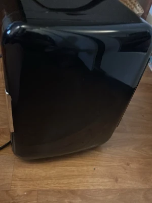 Svart sminkkylskåp med läderhandtag - Stilrent sminkkylskåp i svart blank plast med rundade hörn och ett snyggt brunt läderhandtag på ovansidan. Perfekt för att hålla dina skönhetsprodukter fräscha och svala. Kompakt design som passar bra på sminkbordet. Vet att det finns en till sladd som man kan använda till bilen vet inte just nu var den är just nu men ifall jag hittar den så skriver jag det annars är den i toppen skick har inte kvar lådan till mini kylskåpet.