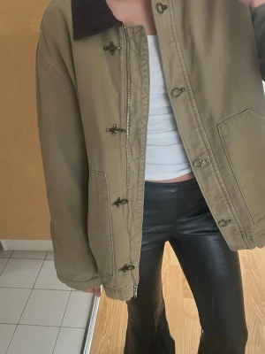 Beige parkajacka med brunt krage - Säljer en beige parkajacka med brunt krage och snygga detaljer som träknappar och dragkedja. Jackan har en loose passform och är tillverkad i ett slitstarkt bomullsmaterial.  Använd ca en gång 