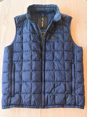 Dunväst från Replay M - Stilren mörkblå dunväst från Replay med quiltat mönster och hög krage. Två sidofickor och en olivgrön insida. Storlek M i bra skick!