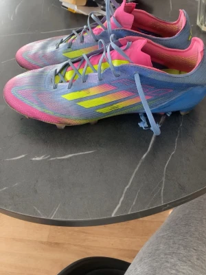 Adidas F50 elite - Säljer ett par Adidas fotbollsskor i en riktigt färgstark design med blå, rosa och gula detaljer. Skorna har snörning, låg profil och är tillverkade i syntetmaterial för lätt vikt och bra bollkontroll. Perfekta för dig som vill sticka ut på planen!