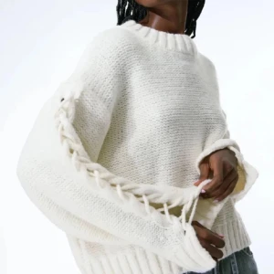 Vit stickad tröja med snörning - Säljer en vit stickad tröja med grov ribbad kant vid hals, ärmslut och nederkant. Tröjan har långärmade ärmar med cool snörningsdetalj längs hela sidan av ärmarna. Passformen är loose och den är perfekt för dig som gillar en chill och trendig look. Pris kan diskuteras vid snabb affär