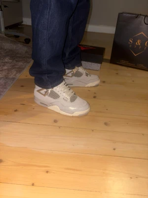 Air Jordan 4 Retro Off White - Säljer ett par Air Jordan 4 Retro frozen moments från Nike. Skorna är i beige och vita toner med meshpaneler, klassiska plastdetaljer och synlig Air-sula. Ikonisk Jumpman-logga på plösen och cool retrovibe. Perfekta för dig som gillar streetwear och sneakerskultur. (Använt de ett par fåtal gånger). Har tyvärr inte kvar kvittot men har kvar låda och påse från butiken.