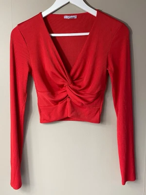 Röd croppad topp - Röd croppad topp med lång ärm och twistad detalj framtill. Ribbad struktur och djup v-ringning.