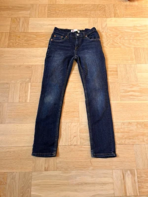 Mörkblå raka jeans från Levi's - Snygga mörkblå jeans från Levi's med klassisk femficksmodell och raka ben. Jeansen har kontrastsömmar, knappgylf och Levi's ikoniska röda etikett på bakfickan. Tillverkade i slitstark denim som passar perfekt till vardagslooken.