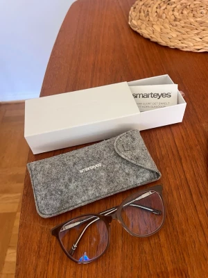 Bruna Smartprotect-glasögon från Smarteyes - Snygga enkelslipade Smartprotect-glasögon från Smarteyes med transparent bruna bågar i plast och metallskalmar. Smartprotect-glaset skyddar ögonen genom en ytbehandling som filtrerar det blåvioletta ljuset, ger ökad kontrast och komfort och minimerar därmed ögontrötthet. Medföljer ett grått fodral i filtmaterial och originalförpackning med kvitto. Perfekt accessoar för att lyfta din stil och skydda ögonen framför skärm.