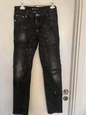 Svarta slim fit jeans med slitningar - Dsquared2 - Säljer ett par svarta slim fit jeans från Dsquared2 med coola slitningar och färgstänk. Jeansen har fem fickor, knappgylf och en röd detalj vid fickan. Materialet är stretchigt denim som sitter snyggt och bekvämt. Perfekta för en trendig streetwear-look.