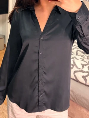 Svart/mörk blå satinblus med knappar🌸 - Stilren svart skjorta i glansigt satinliknande material med klassisk krage och knäppning framtill. Skjortan har långa ärmar med knapp vid manschetten och en avslappnad passform. 