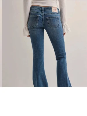 Blå bootcut jeans från True Religion - Snygga blå bootcut jeans från True Religion med klassiska kontrastsömmar och broderade bakfickor. Jeansen har låg midja, fem fickor och stängs med knapp och dragkedja. Perfekta för en trendig och avslappnad look.