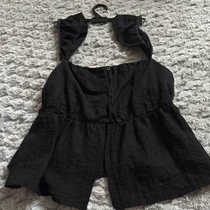 Svart linnetopp med knappar - Snygg svart linnetopp med knappar framtill och breda axelband. Toppen har en luftig passform och är perfekt för varma dagar. Materialet känns lätt och svalt mot huden. Enkel att matcha med både jeans och kjol.
