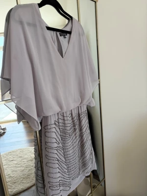 Ljus kortklänning från Warehouse - Säljer en ljus kortklänning från Spotlight by Warehouse. Klänningen har v-ringning, vida ärmar och ett flowy överdel. Kjoldelen har ett diskret mönster i svart och resår i midjan. Perfekt för dig som gillar en luftig och elegant stil. UK size 10