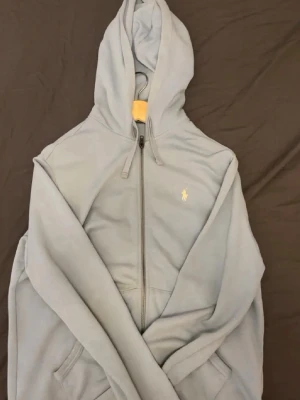 Polo Ralph Lauren Zip Hoodie - Ljusblå zip polo ralph lauren hoodie köpt från boozt 1 år sen, inte anvönd ofta, cond 9/10 bara tvätt behövs.