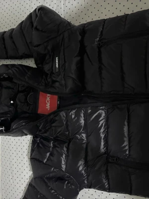 Svart pufferjacka från JACK1T - Snygg svart pufferjacka från JACK1T med glansig finish och vadderad design. Jag köpte jackan för 3000 nypris och säljer den för detta priset. Vid snabbköp var gärna säkra och prisförslag är alltid välkomna 