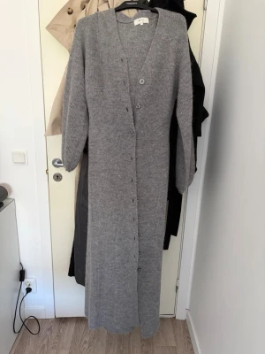 Lång grå stickad kofta från gina - Säljer denna otroligt populära koftan/klänningen från gina, använd endast en gång storlek m