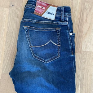  Jacob Cohën Jeans - Säljer ett par riktigt feta Jacob cohen jeans. Dem är kända för sina snygga loggor på baksidan och denna lever upp till förväntningarna. Ända defekten är ett litet hål på höger ben men det ser bara snyggt ut. Längd 107cm Midja 42cm Benöppning nere 18,5cm 