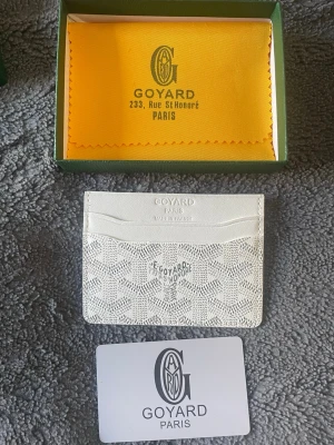 Vit korthållare - Snyggt vitt kortfodral med mönster och präglad logga. Fodralet har flera kortfack och är tillverkat i tåligt canvasmaterial med exklusiv känsla. Perfekt för att hålla koll på dina kort i stil.