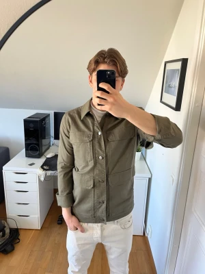 Olivgrön overshirt med fickor - Stilren olivgrön overshirt från Royal Robbins med fyra stora fickor framtill och knäppning hela vägen. Rak passform och klassisk krage. Snygg innerficka. Hör gärna av dig vid frågor!