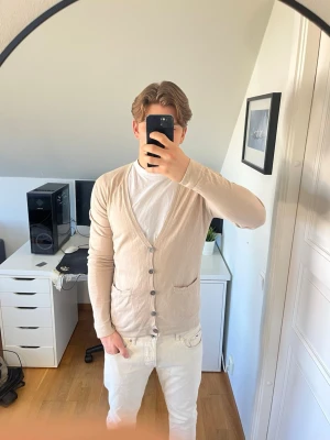 Beige tunn kofta från Filippa K - Snygg beige kofta ifrån Filippa K. Koftan är tillverkad i väldigt mjuk bomull. Det finns en liten fläck på framsidan (se bild 6). Hör gärna av dig vid frågor!