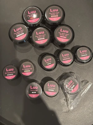 Luu gelé- och spindelgeler för naglar - Flera burkar Luu geléprodukter för naglar, inklusive Non Stick Hard Builder Gel, 3D Painted Gel, Spider Gel och Painting Gel. Förpackningarna är svarta med rosa etiketter. Perfekt för kreativa nageldesigner och konstnärliga effekter.