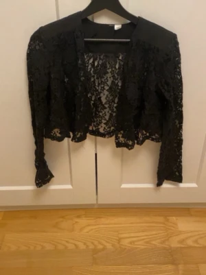 Svart spetskofta - Säljer en svart långärmad spetsbolero. Kortare modell som ger en snygg layering-effekt till din outfit. Perfekt för att addera lite edge och elegans till din look.