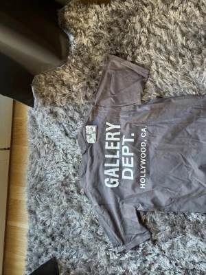 Grå t-shirt från Gallery Dept. - Säljer en grå t-shirt från Gallery Dept. med tryck i vitt på ryggen och bröstet. T-shirten har klassisk passform och korta ärmar. Perfekt för dig som gillar streetwear och vill ha något stilrent men ändå med edge. Känns som XS 