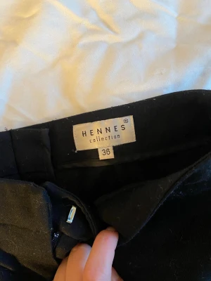 Svarta kostymbyxor från Hennes - Snygga svarta kostymbyxor från Hennes collection med en liten utsvängd modell. Byxorna har diskreta fickor fram och stängs med hake och dragkedja. Perfekta till en stilren look och passar till många olika outfits.