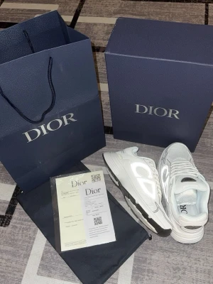 Dior b30 - Snygga vita sneakers från Dior med reflekterande silverdetaljer på sidorna och svart sula. Skorna har en modern och chunky design med mesh och lädermaterial. Perfekta för dig som vill sticka ut med exklusiva och trendiga sneakers.