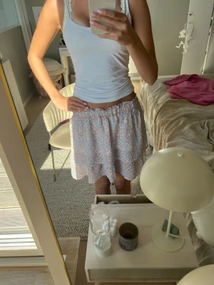 Blommig volangkjol i pastellfärger - Söt kortkjol med blommigt mönster i ljusa pastellfärger. Kjolen har volangkant och resår i midjan för en bekväm passform. Perfekt för vår och sommar, lätt och luftig i materialet.