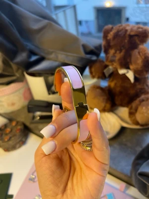 Guldpläterad armband med rosa emalj 16cm - Snyggt armband i guldfärgad metall med rosa emaljpaneler och ett H-format spänne. Armbandet har en modern och stilren design som passar perfekt till trendiga outfits. Perfekt accessoar för dig som gillar att sticka ut med detaljer.